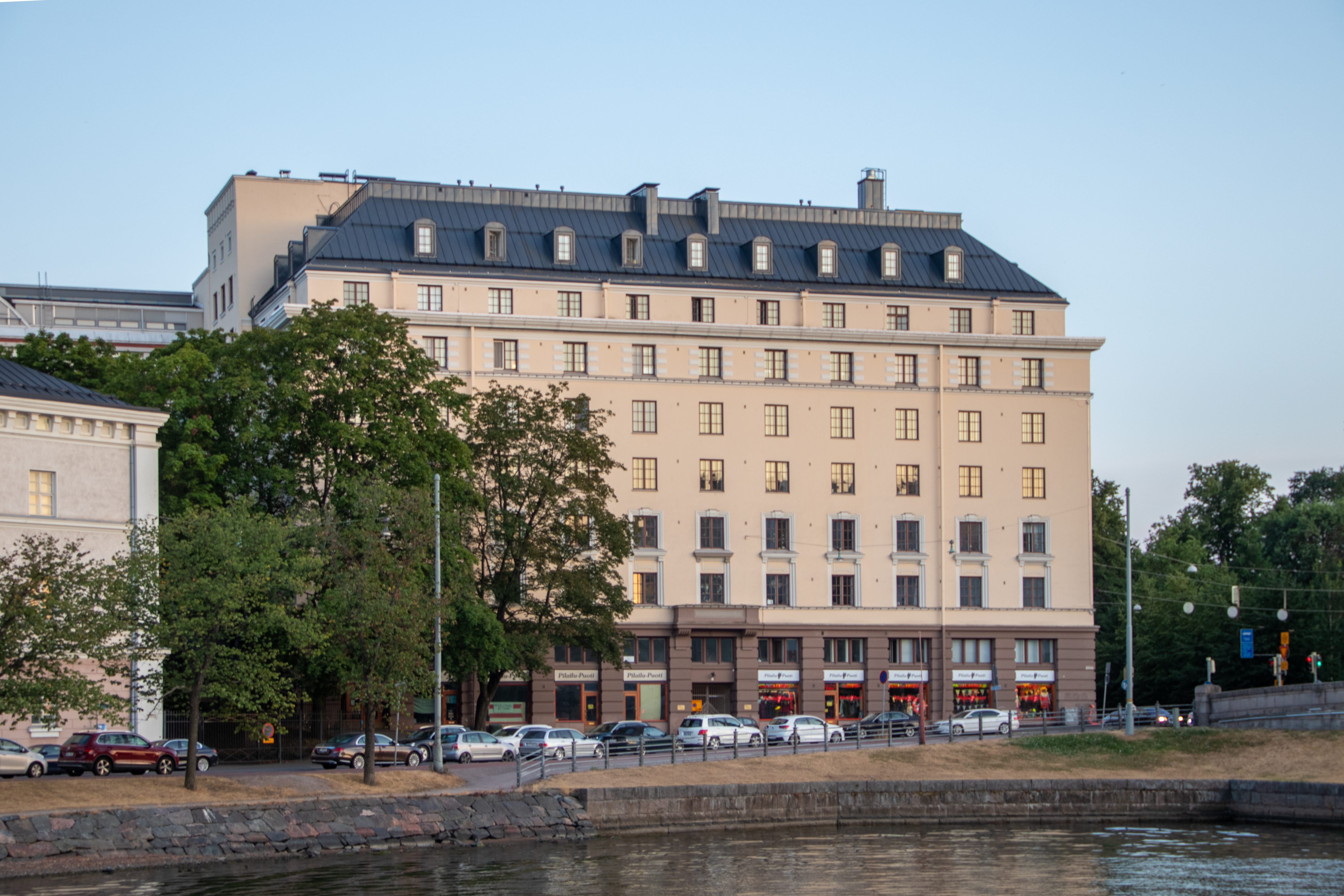 Asuinkerrostalo Unioninkadun päässä Kruununhaassa Helsingissä, ilta-aurinko vaalealla julkisivulla ja meren ranta etualalla